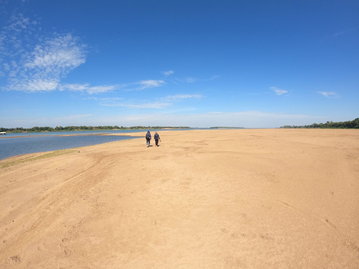 Two people walking along large sand bar in Cambodia
